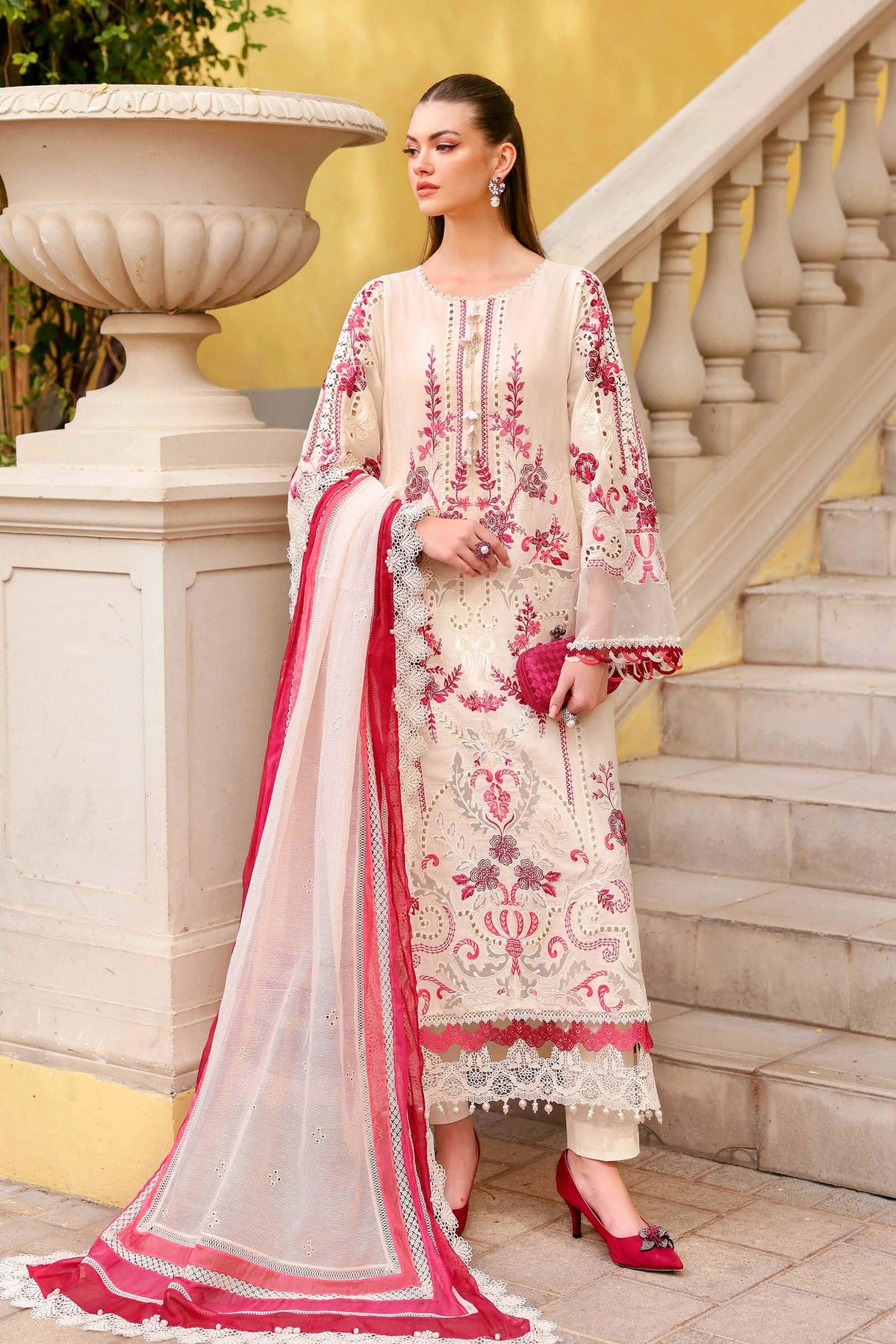 Woman in a traditional embroidered outfit standing on steps with a yellow wall in the background