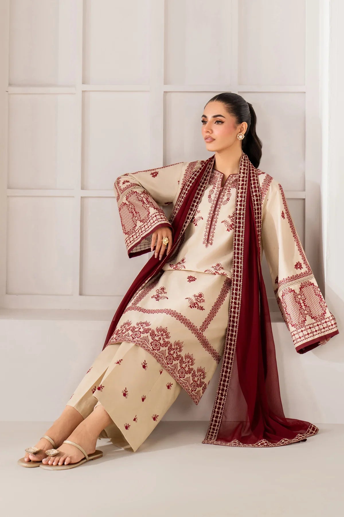 Woman wearing a traditional outfit with red and beige patterns against a white wall.
