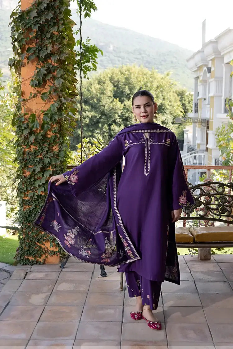 Woman in a purple traditional outfit standing outdoors with greenery and a building in the background